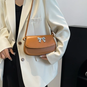 Close-up of caramel leather shoulder bag with a silver metallic bow and flap cover