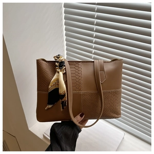 Detail of snake pattern leather texture and silk scarf handle on brown tote bag