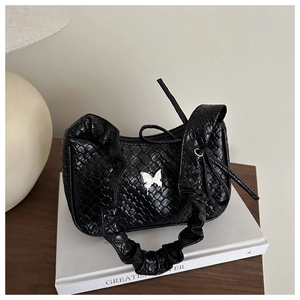Détail d'un sac à main noir avec charm papillon argenté et bandoulière froncée