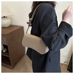 Detail of beige crocodile embossed leather shoulder bag with gold text and knot accents