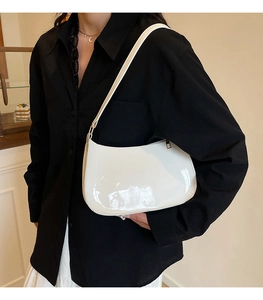 Close-up of a white semi-circle underarm bag in glossy patent leather on shoulder