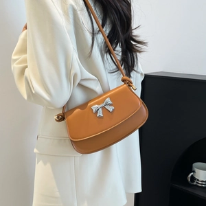 Detail of tan leather crossbody bag featuring a silver bow buckle and sleek oil edge finish