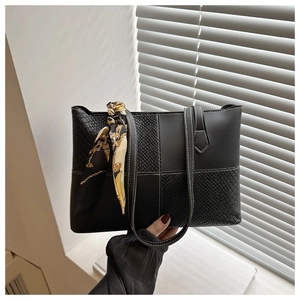 Close-up of black tote bag with croc-embossed leather panels and a yellow printed silk scarf