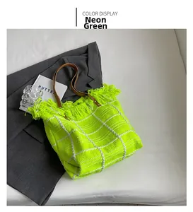 Detail of neon green woven tote bag with fringe edge and brown leather shoulder strap