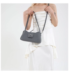Detail of grey baguette bag with silver metal bow and textured leather material