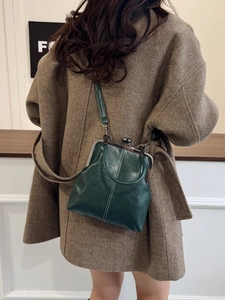 Detail of dark green vintage kiss-lock bag worn as a crossbody on a brown plaid coat