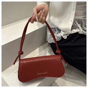 Detail of dark red crocodile textured handbag with golden FASHION & BAGS lettering