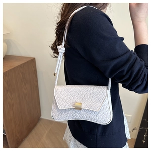 Detail of cream shoulder bag featuring woven texture and knot handle on model