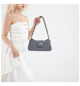 Detalle del bolso baguette gris con lazo plateado y textura de tela de grano elegante