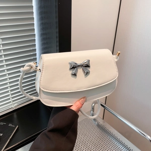 Detail of a creamy white shoulder bag featuring a silver metal bow on smooth synthetic leather