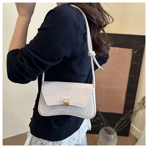 Detail of white woven texture shoulder bag with golden magnetic buckle and knot strap