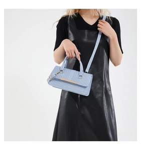 Close-up of a light blue textured handbag with golden metal bar and long shoulder strap