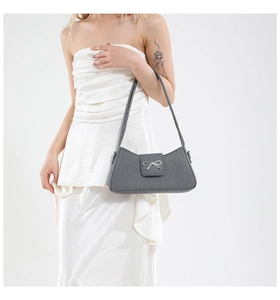 Vista detallada del bolso baguette gris con hebilla de lazo plateada y textura de tela suave