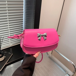 Detail of fuchsia leather handbag featuring a silver metallic bow and curved flap