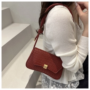 Detail of brick red crocodile texture underarm bag with gold clasp on white outfit