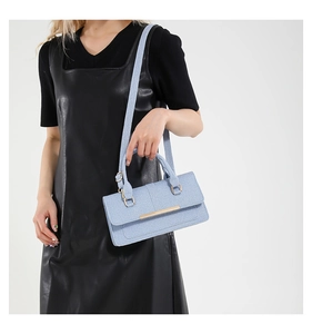 Detail of light blue textured crossbody bag with gold hardware shown on a female model