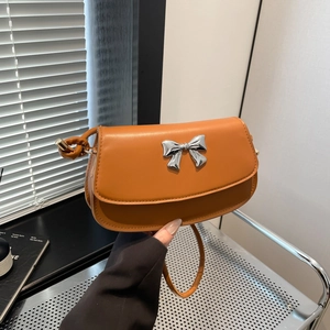 Close-up of caramel leather shoulder bag featuring a silver metal bow and knotted strap details