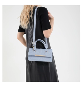 Close-up of light blue woven handbag with gold accents held by model in leather dress