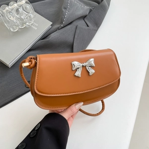 Detail of silver bow accent on brown leather flap bag with precise stitching
