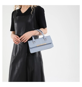 Detail of light blue textured handbag with gold metal bar and top handle grip
