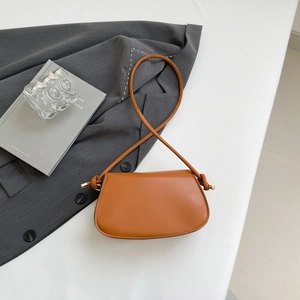 Close-up of brown leather shoulder bag featuring a knotted strap detail on white surface