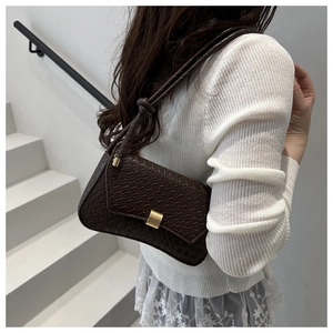 Detail of dark brown woven underarm bag featuring a metallic buckle on a model