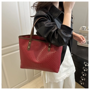 Detail of woven texture tote bag in deep red with leather straps and metal rivets