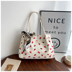 Detail of white corduroy tote bag with red strawberry print and woven handle with scarf
