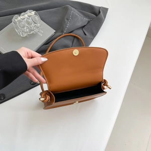 Detail of warm brown leather shoulder bag featuring a light gold magnetic clasp and black lining