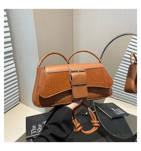 Close-up of brown crocodile texture flap bag with decorative wide buckle and knotted strap