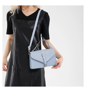 Detail view of light blue knitted fabric handbag with golden U-shaped buckle and strap