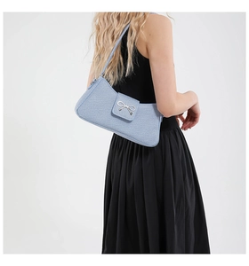 Détail du sac porté épaule en denim bleu clair avec un nœud décoratif en métal argenté