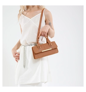 Brown leather crossbody bag with gold metal trim shown on model with white silk outfit