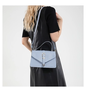 Close-up of light blue crossbody bag featuring woven texture and metallic U-shaped buckle