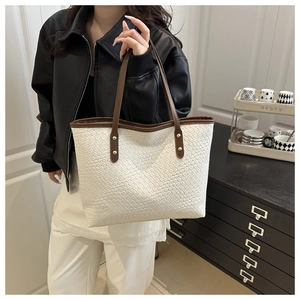 Detail of woven texture on cream tote bag with brown straps and gold rivets