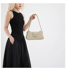 Détail du sac baguette tissé or clair avec boucle nœud argentée sur robe noire