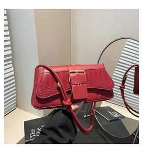 Detail of red crocodile pattern shoulder bag with a gold buckle and knotted strap