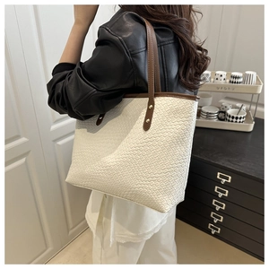 Detail shot of a white woven texture tote bag with brown straps worn on a shoulder