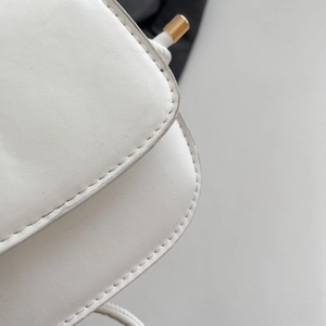Detail view of white textured leather material with clean stitching and gold metal hardware
