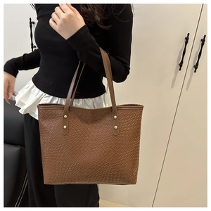 Detail showing the woven texture of the brown tote bag and gold metal rivet accents