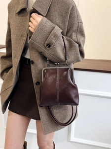 Detail of vintage dark brown leather frame handbag with white stitching on plaid coat