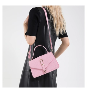 Pink textured crossbody bag with metal buckle and shoulder strap shown on model