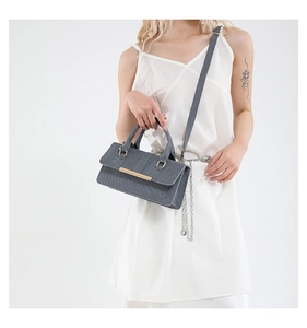 Close-up of grey rectangular crossbody bag with gold hardware and wide woven strap