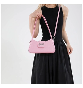 Pink underarm bag with silver bow buckle worn by model against a white background