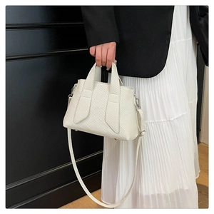 Detail of white textured tote bag with silver hardware held by model in black suit