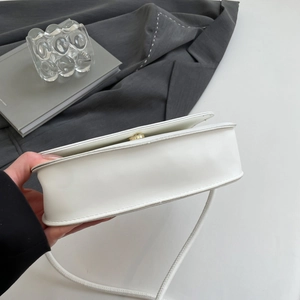 Detail view of white leather shoulder bag featuring a sleek gold metal lock and strap