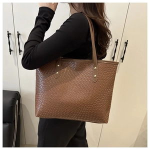 Brown woven texture tote bag with gold rivets shown on a model in a modern interior