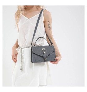 Crossbody view of a gray textured small square bag with V-shaped flap and metal buckle