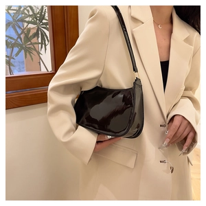 Close-up of black patent leather underarm bag with glossy finish on beige blazer