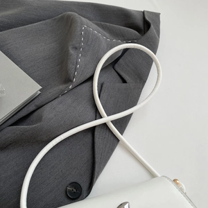 Close-up of white leather crossbody bag paired with a textured grey blazer and metal buckle